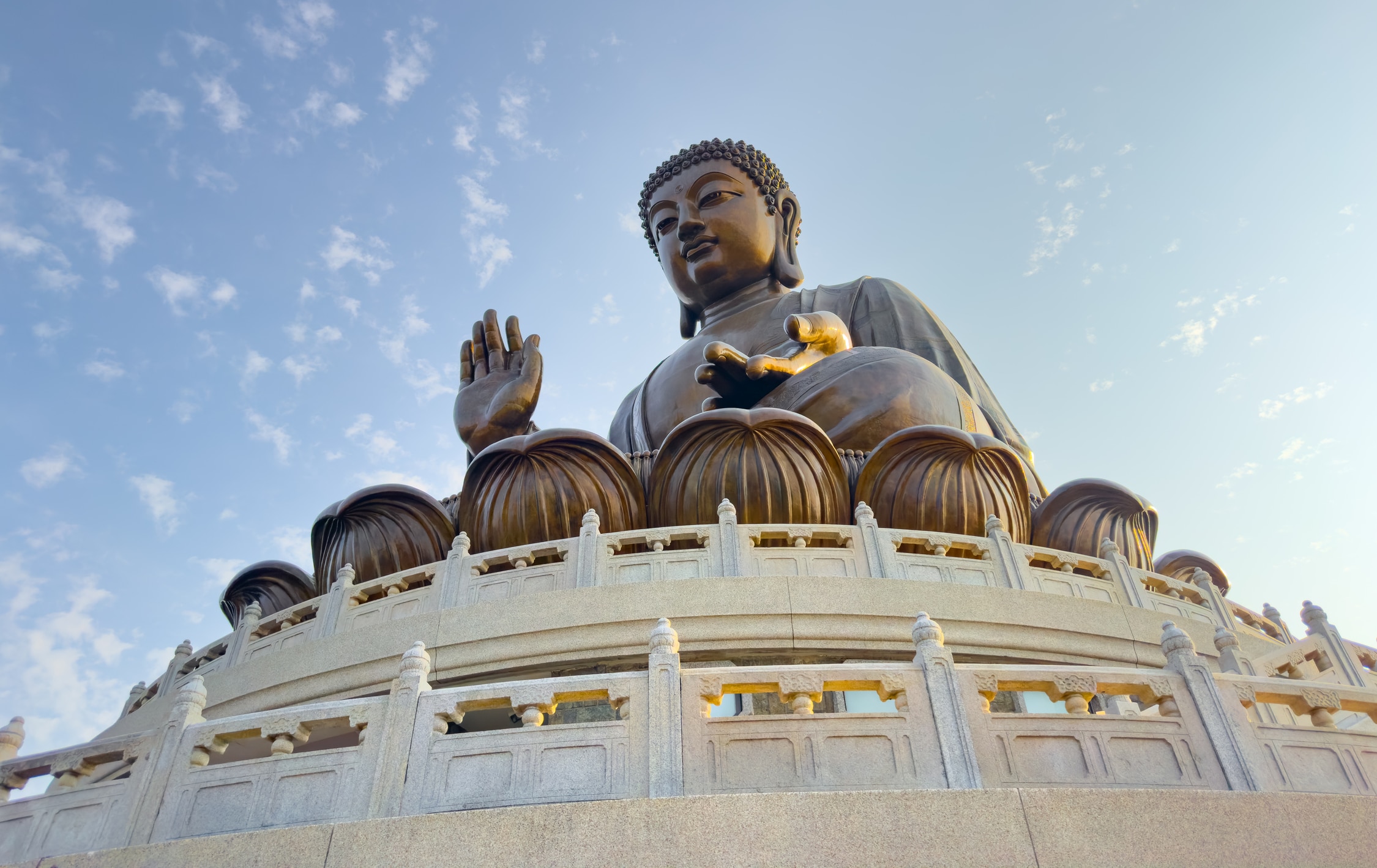 Die Buddha Statue auf ihrem Sockel steil von Unten fotografiert. Von der Sonne angestrahlt erkennt man gut die Bronzefarbe.